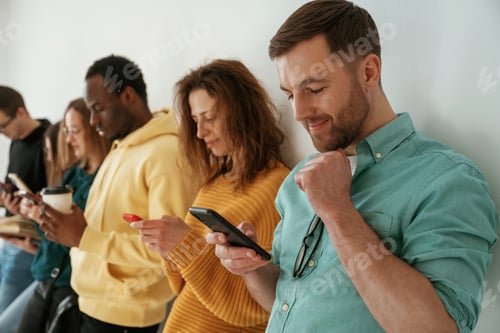 Preview: Busy by using smartphones. Group of young people are standing against white background