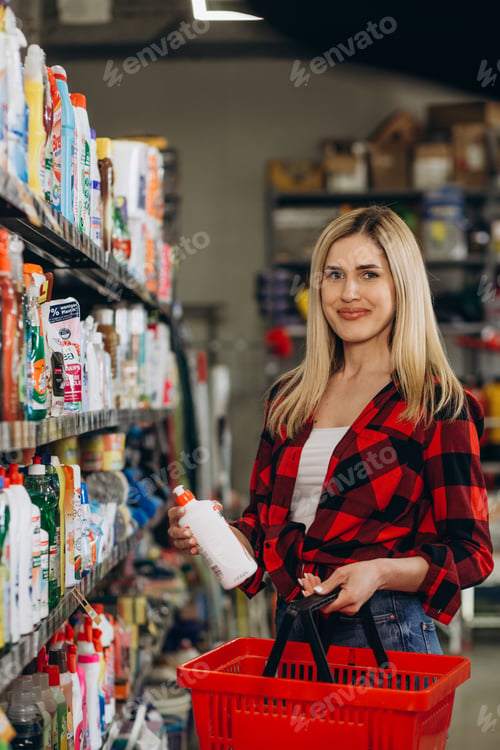 Preview: Interested young woman making purchases in household chemicals store, reading labels on bottles.