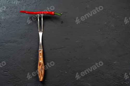 Preview: Red chili pepper on fork on black stone background