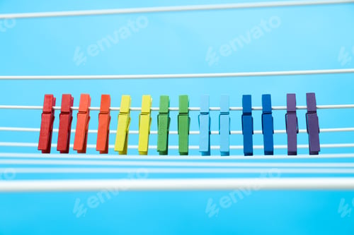 Preview: Multicolor clothespins hanging on drying rack on blue background