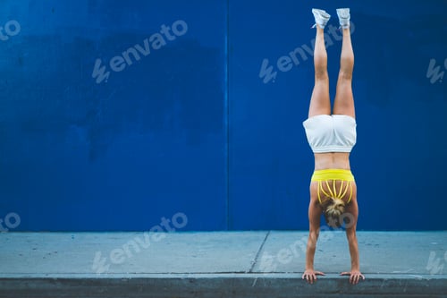 Preview: Young woman doing handstand outdoors in front of blue wall