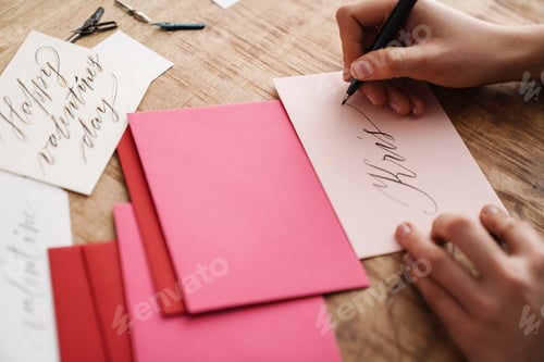 Preview: Calligrapher girl writing while working on valentines at table indoors