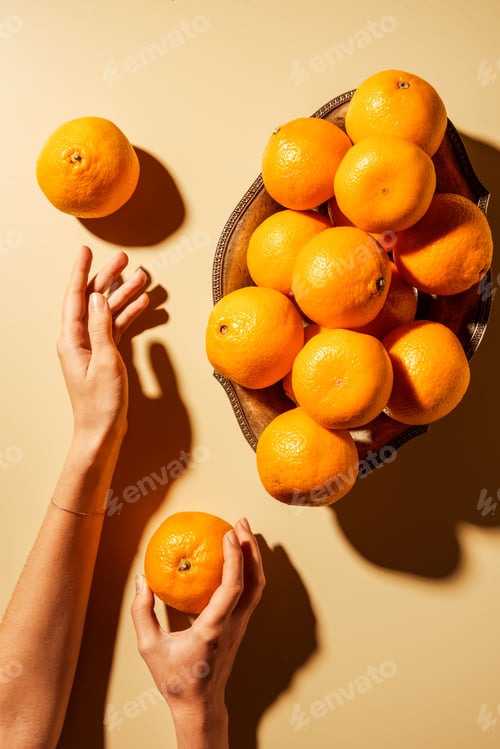 Preview: Cropped shot of woman holding tangerine on beige background with metal bowl