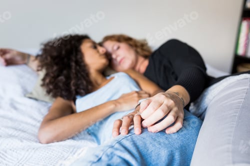 Preview: Two women lying down on bed and cuddling