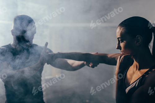 Preview: man training beautiful young sportswoman in smoke