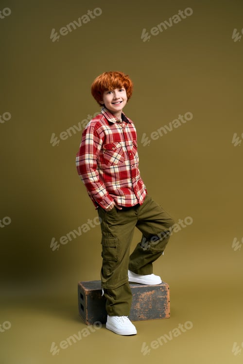 Preview: Stylish little boy poses confidently in trendy outfit against a warm background