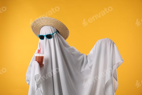Preview: Person in ghost costume, sunglasses and straw hat holding glass of drink on yellow background