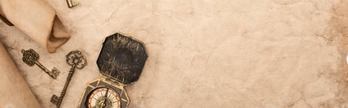 Preview: top view of vintage keys and compass on aged paper, panoramic shot