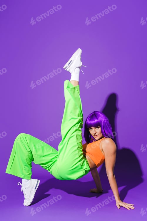 Preview: Carefree woman dancer wearing colorful sportswear having fun against purple background