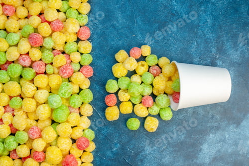Preview: Overhead view of colorful sweets poured out from small white pot and on the blue background