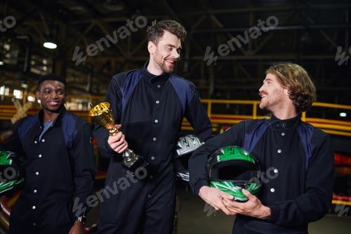 Preview: excited man holding golden cup and standing as a winner of go-kart race near diverse drivers