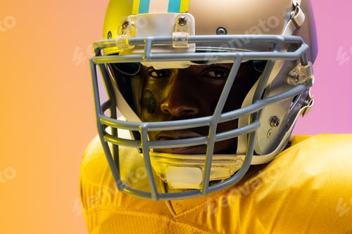 Preview: African american male american football player wearing helmet with neon yellow and purple lighting