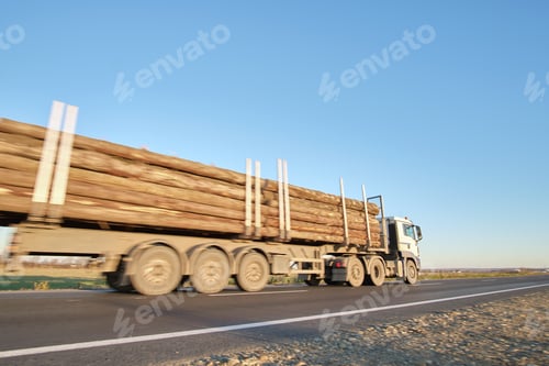 Preview: Semi-truck with cargo trailer driving on highway hauling cut down trees in evening. Timber delivery