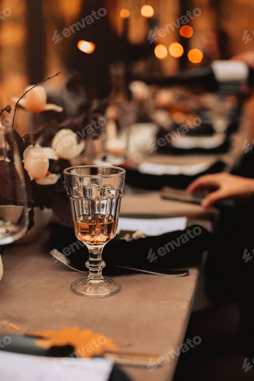 Preview: Selective focus on tall glass with white wine standing on dinner table after festive banquette