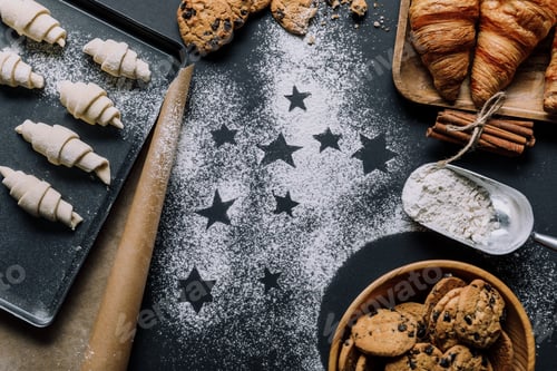 Preview: top view of tray with dough for croissants on surface covered by flour with symbols of stars