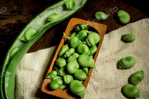 Preview: Top view shot of fresh raw broad beans in the pod and a pile of beans in the wooden dish