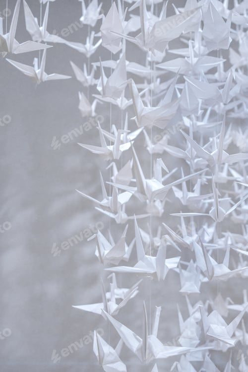 Preview: Hundreds of white origami cranes suspended in midair against a white background.