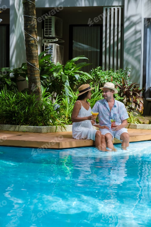 Preview: Men and women with hat drinking cocktails by the pool during vacation