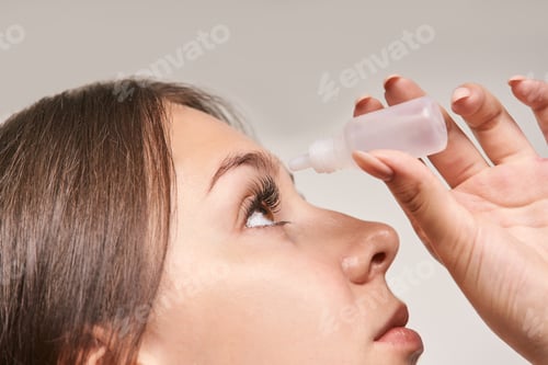 Preview: Young caucasian female applying eye drops close-up side view focused relief