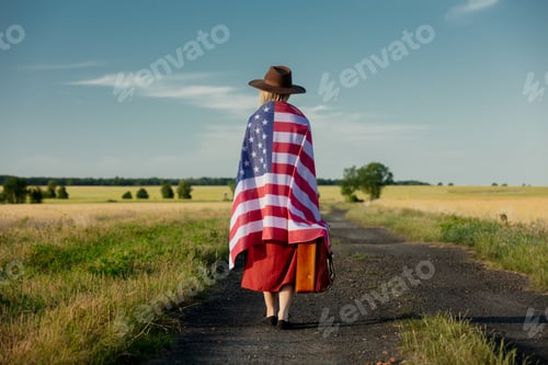 Preview: Girl in USA flag with suitcase on country road in sunset