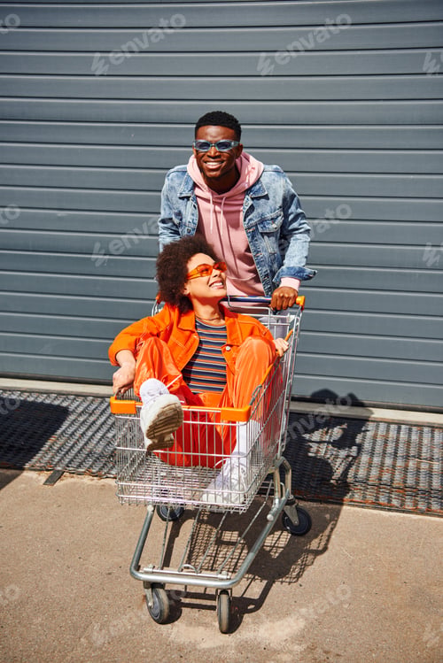 Preview: Smiling young african american man in denim jacket and sunglasses standing near best friend