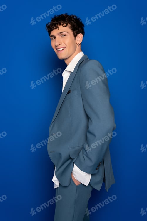 Preview: Positive model in suit and shite shirt looking at camera on blue background