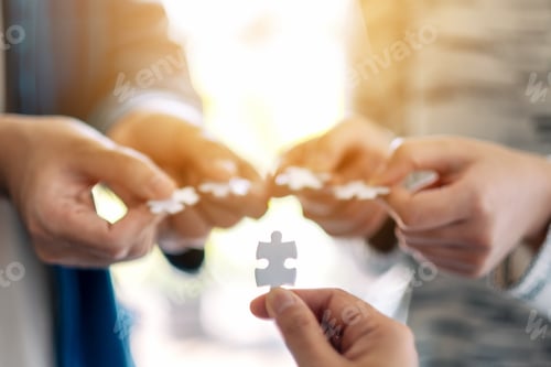 Preview: Closeup image of many people holding and putting a piece of white jigsaw puzzle together