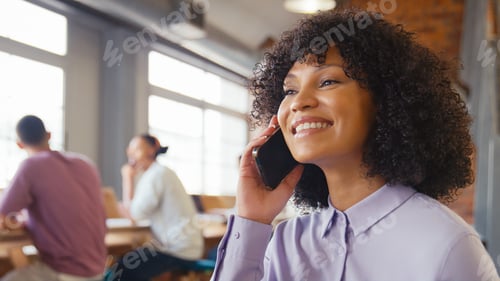 Preview: Businesswoman Talking On Mobile Phone In Busy Open Plan Office With Colleagues In Background