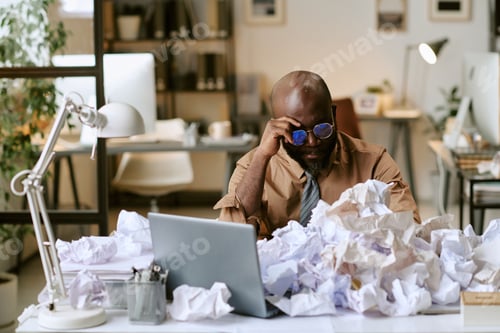 Preview: Black Man Experiencing Work Overload Surrounded by Crumpled Papers