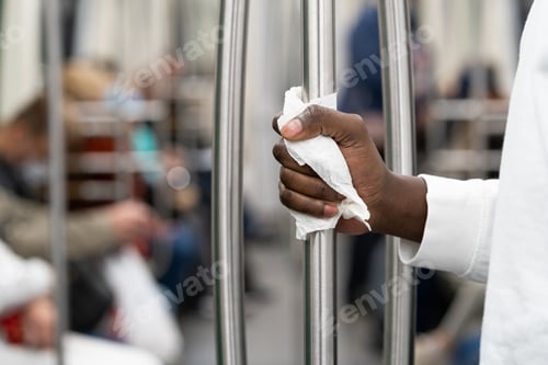 Preview: Black man hand holds a handrail in public transport or subway through a napkin. New normal, Covid-19