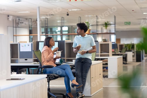 Preview: Young biracial colleagues discussing while eating lunch together in cubicle at modern workplace