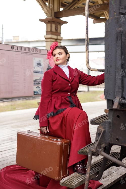 Preview: A girl in a burgundy suit and a hat stands with a suitcase near an old steam locomotive.Vintage