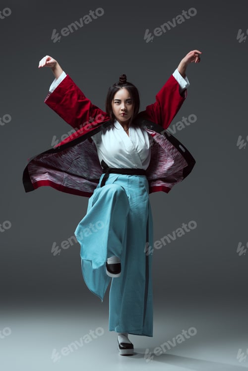 Preview: full length view of asian woman in traditional japanese kimono looking at camera on grey