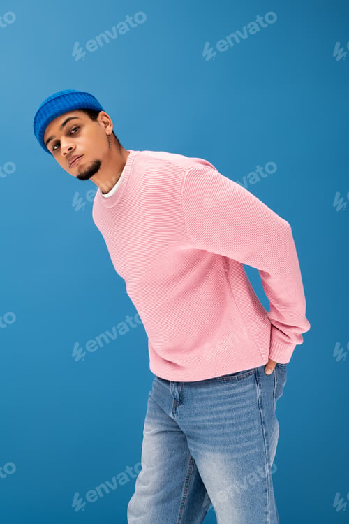 Preview: Young man showcases trendy style against blue backdrop in modern fashion scene