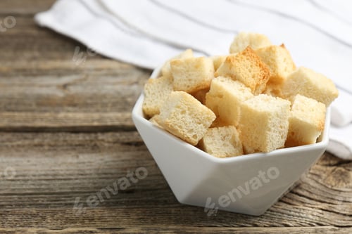 Preview: Tasty crispy croutons in bowl on wooden table, closeup. Space for text