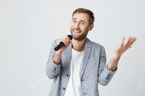Aperçu: Mannequin masculin talentueux portant une veste grise élégante tenant un micro et chantant des chansons tout en posant
