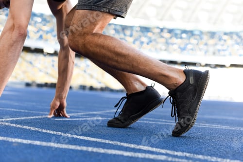 Preview: cropped view of runner in start position on running track at stadium