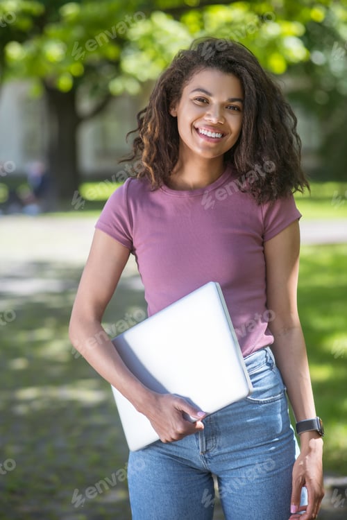 Preview: A cute girl in a pink tshirt with a laptop smiling nicely
