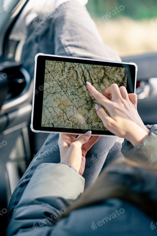 Preview: A girl sits in a car in the front passenger seat with a cup of tea and plots a route through forest