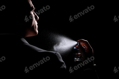 Preview: Man spraying luxury perfume on black background, closeup
