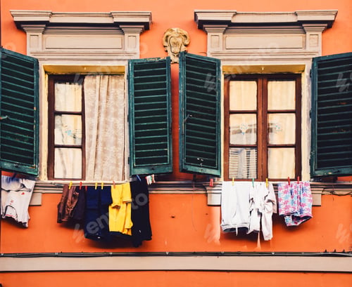 Preview: old orange building with two windows with shutters and laundry hanging drying under windowsills