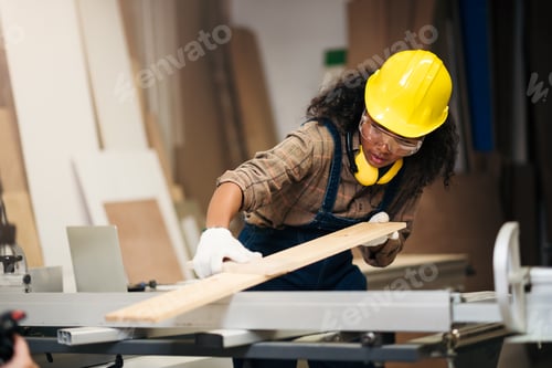 Preview: Young black female carpenter wearing safety goggles and hard hat for woodworking in small business