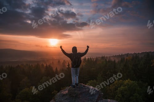 Preview: The young man stands on a rock looking at the sunrise in the countryside.