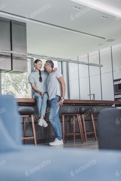 Aperçu: low angle view of attractive woman sitting on kitchen counter and embracing boyfriend at home