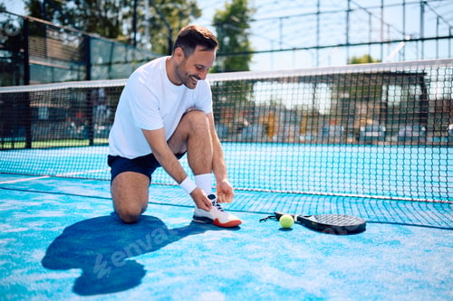 Preview: Happy athlete tying shoelace while playing paddle tennis on the court.