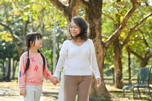 Preview: Smiling middle age grandmother and cute granddaughter walking in public park at morning.