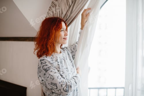 Preview: Red-haired woman opening curtains, welcoming morning light