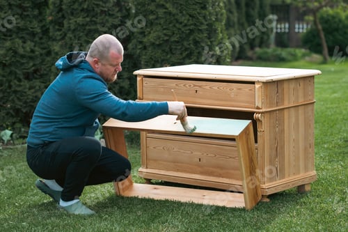 Preview: Man painting a wooden furniture while sitting with hir dog in the garden. DIY concept.