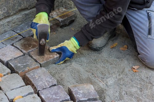 Preview: The master in gloves lays paving stones in layers stone road by professional paver worker