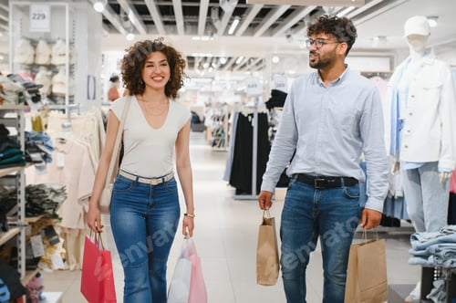 Preview: Happy couple carrying shopping bags in clothing store